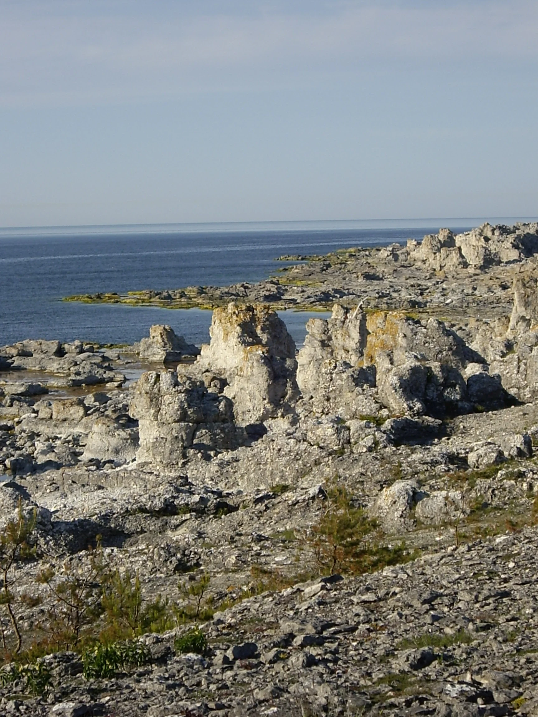 Rocky coast with jagged formations stretches toward calm blue water under a clear sky.