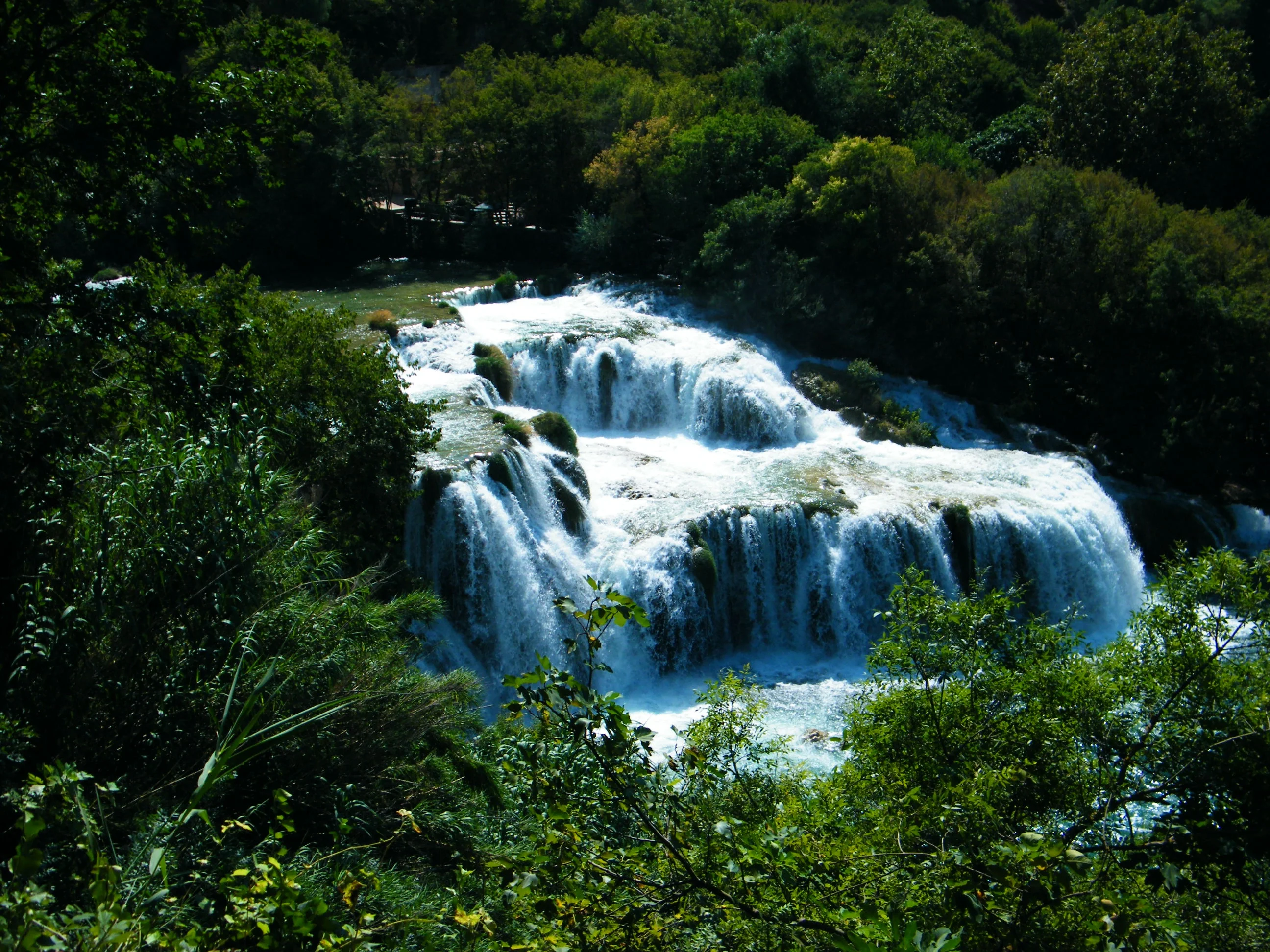 Water cascades down multiple tiers, surrounded by lush greenery.