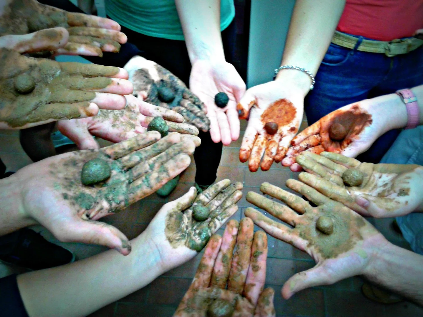 Several hands hold colorful mud balls, forming a circle of creative expression.