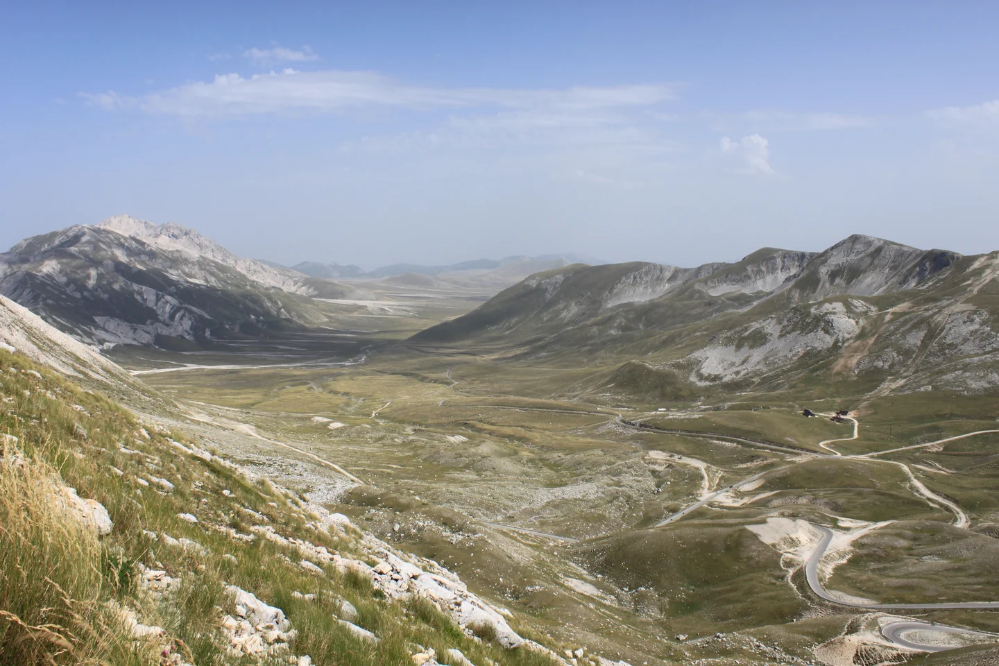 Wide valley flanked by rocky hills with curving road and distant vehicles.