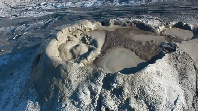 Volcanic crater surrounded by rugged terrain and icy patches.