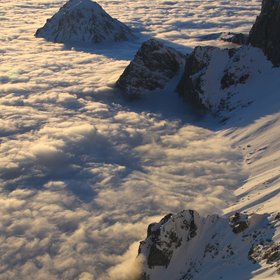 A sea of clouds bracking against snow-covered mountains