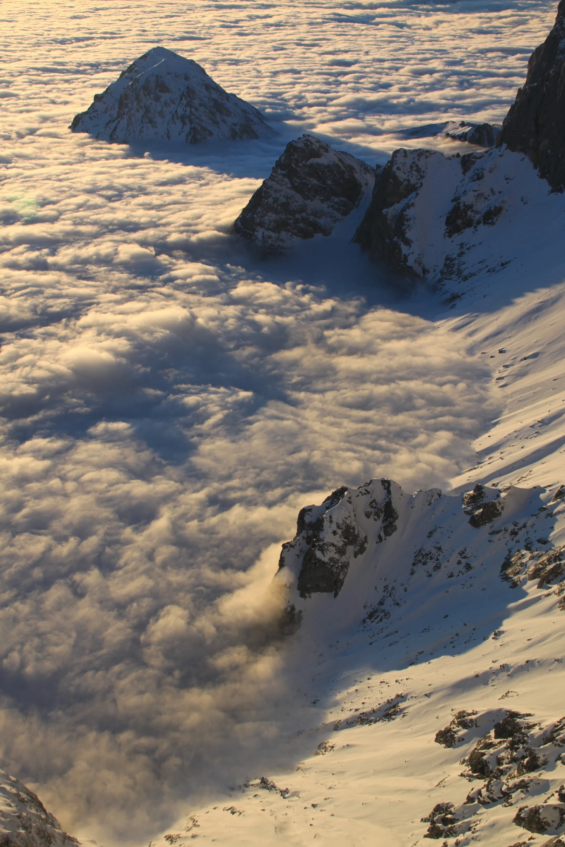 A sea of clouds bracking against snow-covered mountains