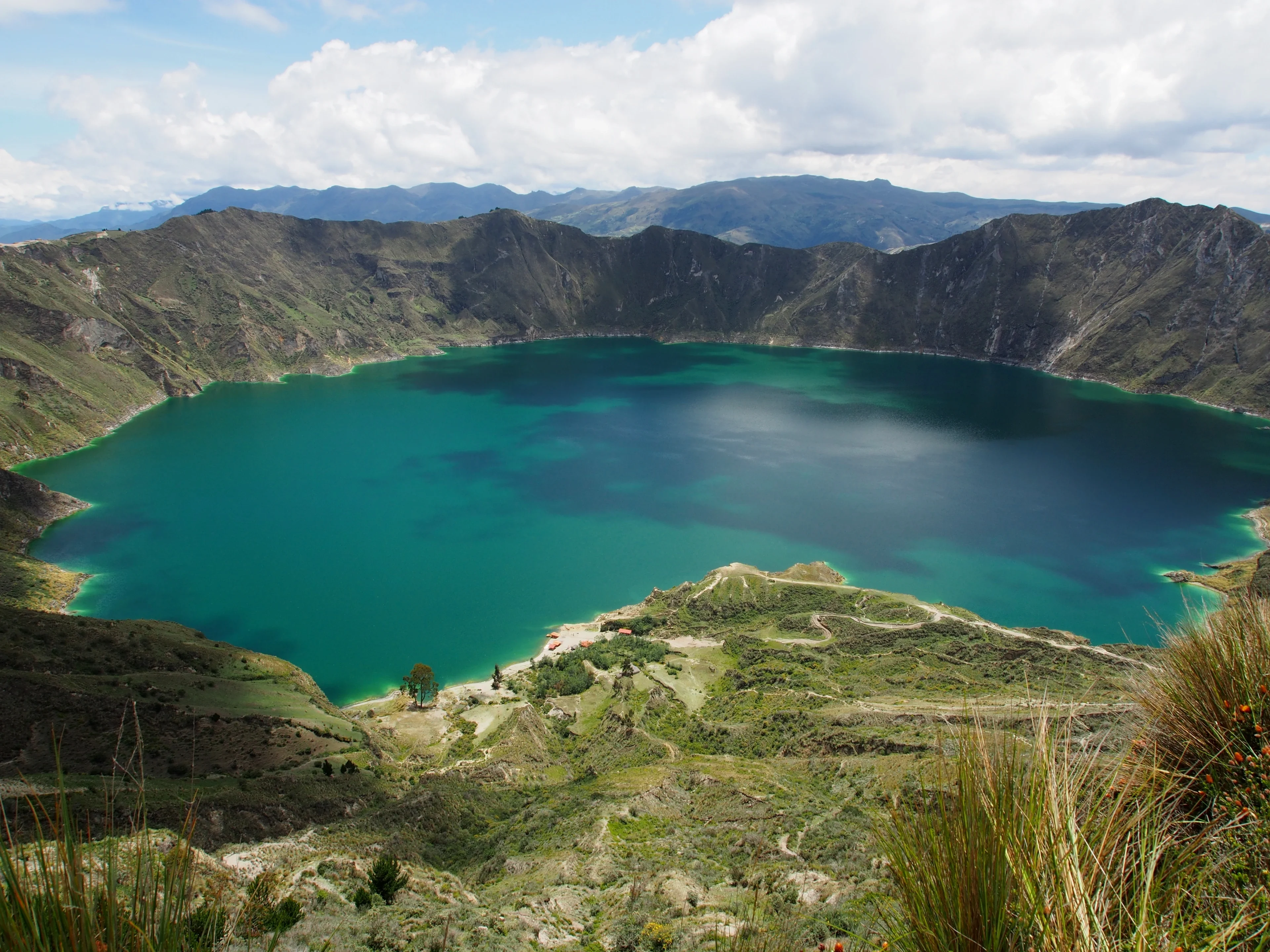 A serene lake surrounded by lush green mountains under a partly cloudy sky.
