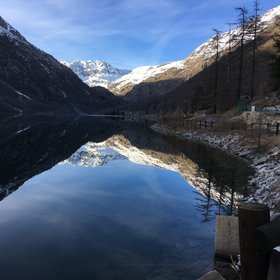 Ceresole Reale ice-free lake acting as a perfect mirror during sunny winter day.