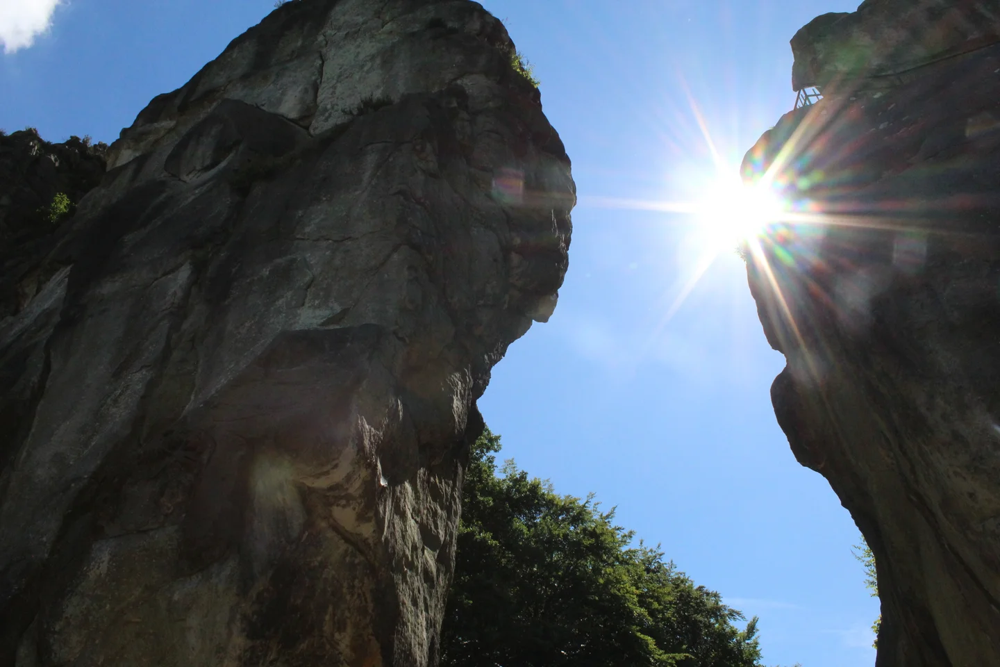 The sun shines brightly between towering rock formations under a clear sky.