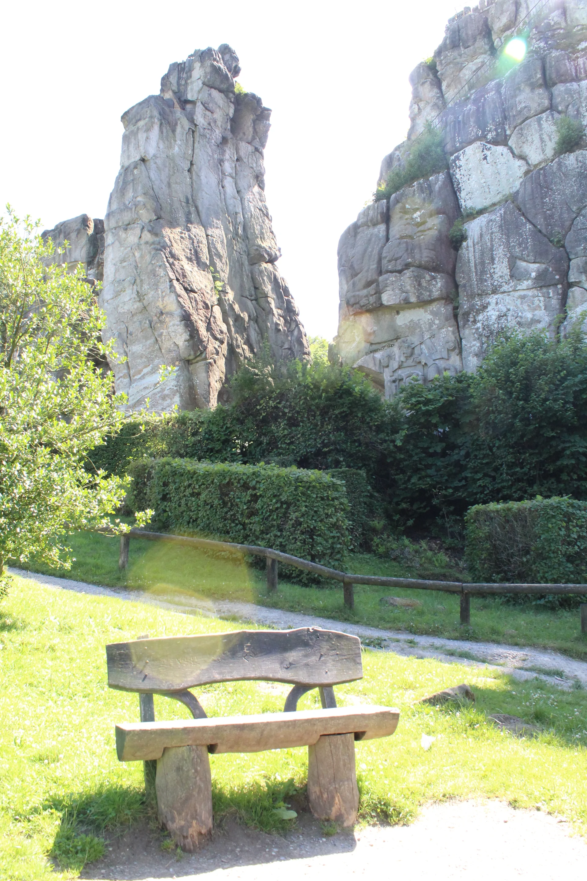 Wooden bench sits on grass near stone formations and greenery.