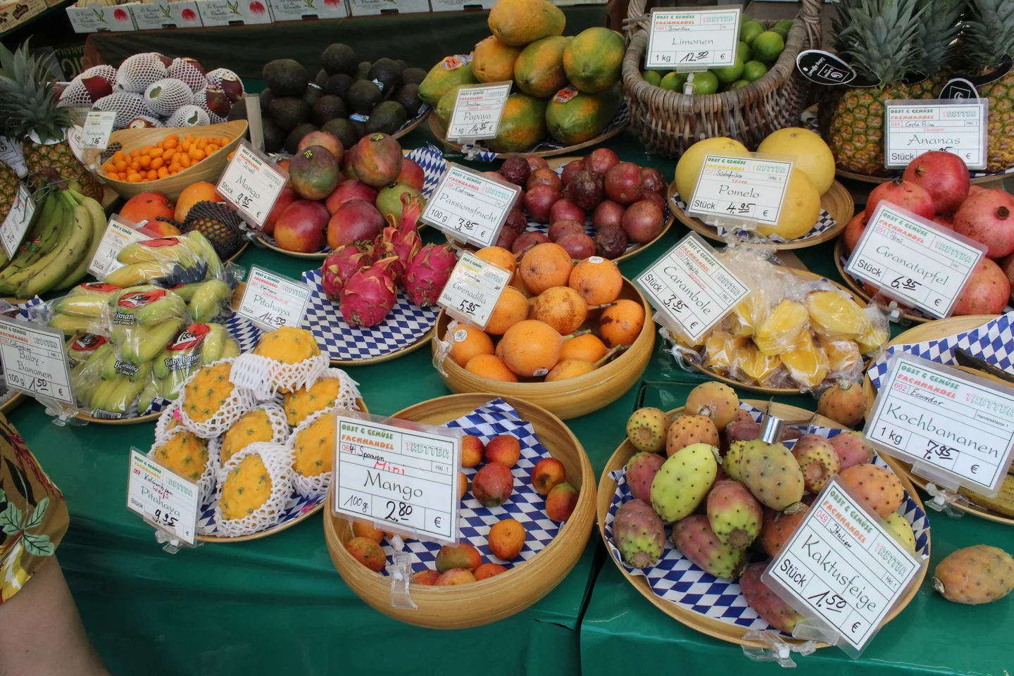 Colorful fruit varieties displayed on a green table with price tags.