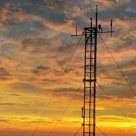 A summit meteorological tower standing as a silhouette against a vibrant sunset