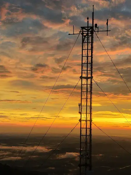 A summit meteorological tower standing as a silhouette against a vibrant sunset