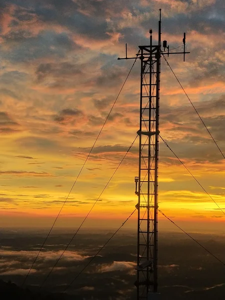 A summit meteorological tower standing as a silhouette against a vibrant sunset