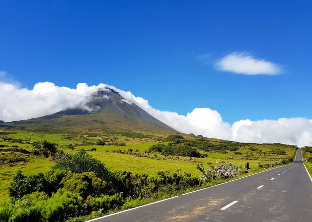 Winding road leads towards a mountain under a bright blue sky.