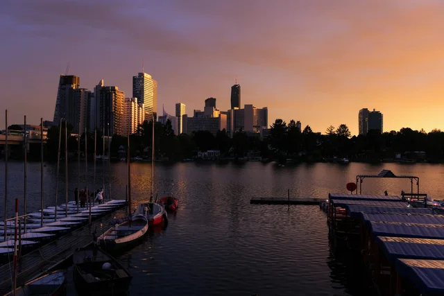 A tranquil dock reflects the warm glow of a sunset over a city skyline.