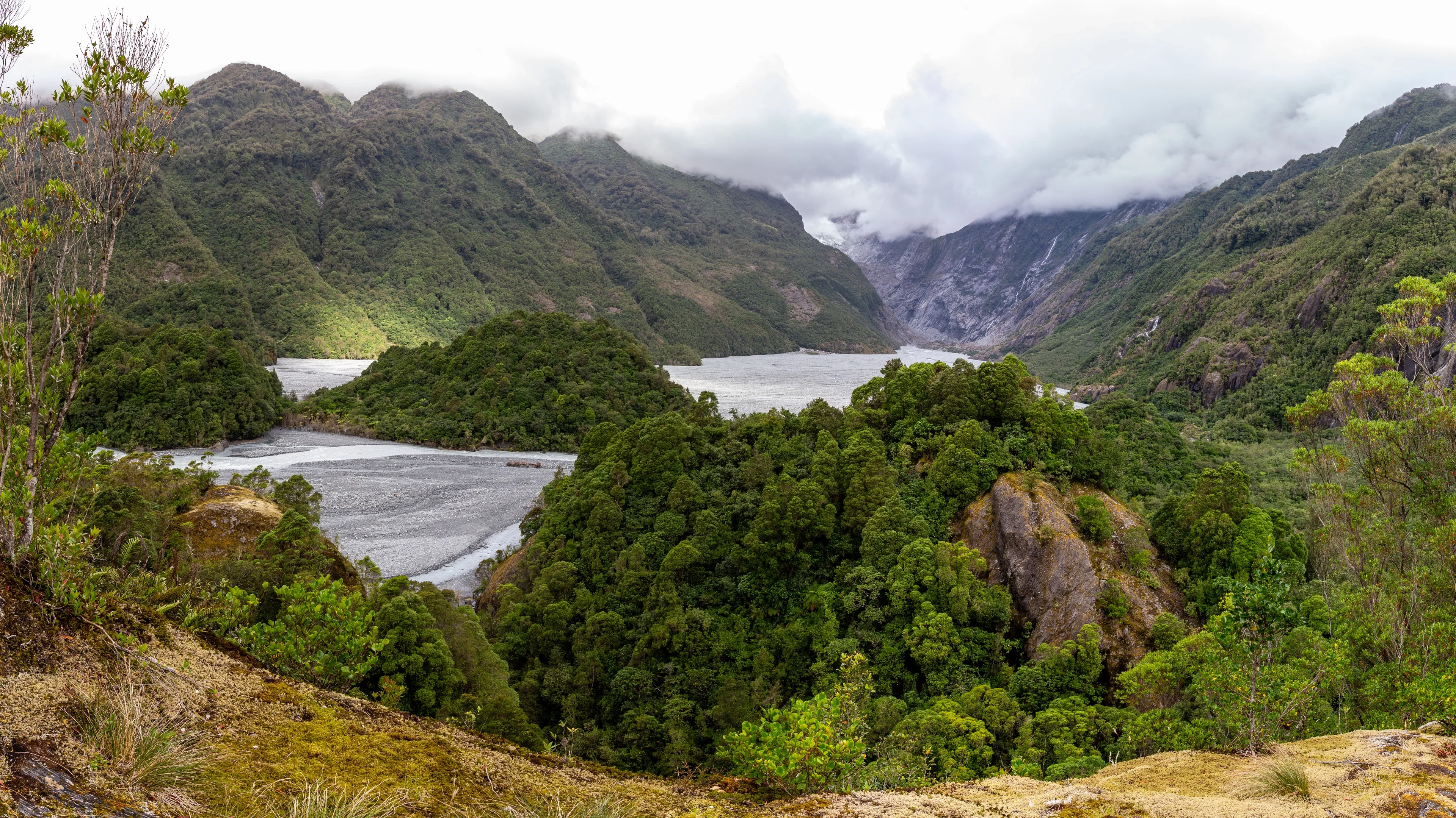 A serene valley with a calm lake, lush forests, and misty mountains in the distance.