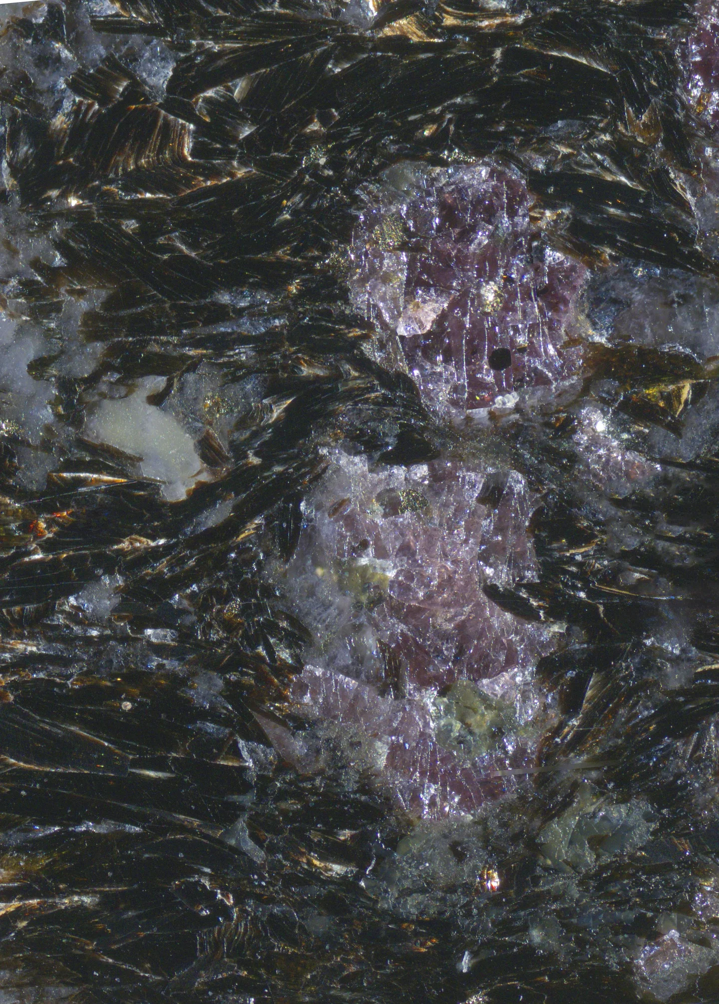 Close-up of colorful crystals, with pink and purple formations surrounded by dark, shimmering minerals.